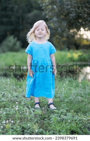 little fair-haired 3-year-old girl in a linen dress shows emotions, children's emotions on a walk, cheerful happy childhood
