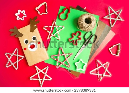 Handmade festive gift wrapping on a red background.  Craft a deer and stars from paper, scissors and colored paper.  Conceptual gifts for Christmas and New Year.  Flat layout.  Background picture.