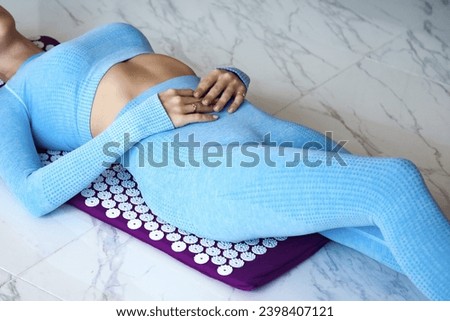 Slim woman in blue sportswear doing body self health massage, back buttocks acupressure mat. Photo of lady lying on orthopedic acupressure therapy. Home healthcare medical concept. Copy ad text space