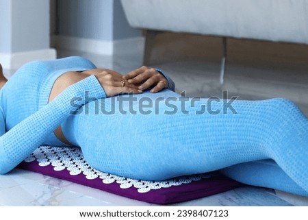 Adult woman doing body self health massage, back acupressure mat therapy. Cropped photo of lady in blue sportswear lying on orthopedic acupressure. Home healthcare medical concept. Copy ad text space