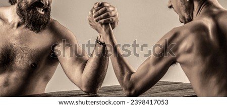 Arms wrestling thin hand, big strong arm in studio. Two man's hands clasped arm wrestling, strong and weak, unequal match. Heavily muscled bearded man arm wrestling a puny weak man.