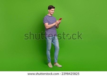 Full size photo of intelligent optimistic guy dressed striped t-shirt jeans read sms on smartphone isolated on green color background
