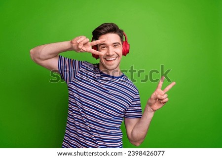Photo of carefree cheerful person enjoy music headphones dance show v-sign near eye isolated on green color background