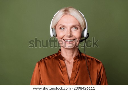 Photo of toothy beaming smart woman dressed silk shirt in headphones answer on customer questions isolated on green color background