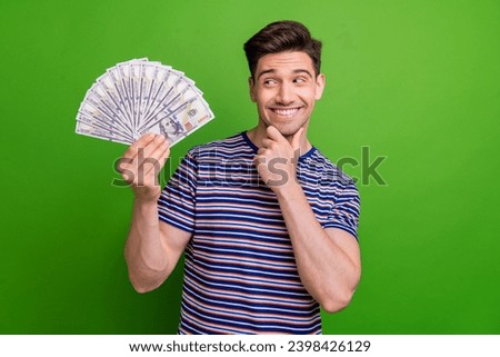 Photo of clever intelligent guy with stubble dressed striped t-shirt get salary look at money in hand isolated on green color background