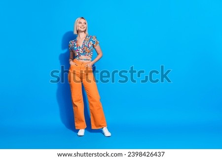 Photo of cheerful positive woman dressed print blouse hands in pockets look at promo empty space isolated on bright blue color background