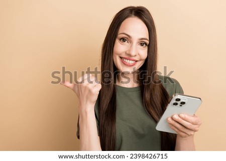 Portrait of young lady directing finger empty space like choosing clothes to buy online use cellphone isolated on beige color background