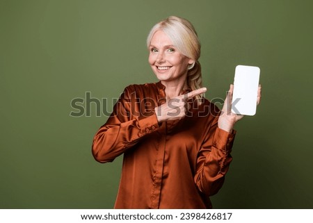 Photo of smart cheerful woman dressed silk shirt directing at eshop on smartphone screen empty space isolated on green color background