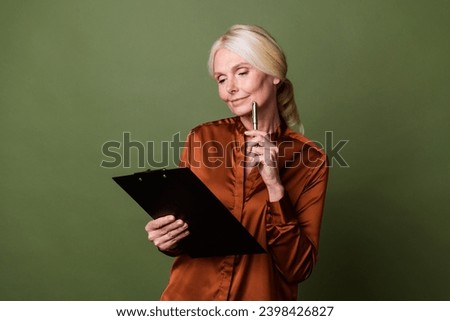 Photo portrait of attractive pensioner woman think look paperholder dressed stylish brown silk clothes isolated on khaki color background