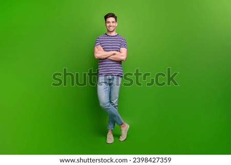 Full size photo of cool pleasant guy dressed striped t-shirt jeans standing holding arms crossed isolated on green color background