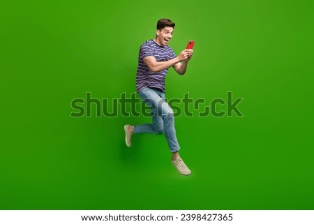 Full size photo of ecstatic crazy guy flying staring at smartphone enjoy unbelievable internet speed isolated on green color background