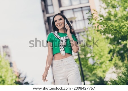 Photo of cute adorable girl dressed green top walking speaking apple samsung iphone modern gadget walking outdoors urban town park
