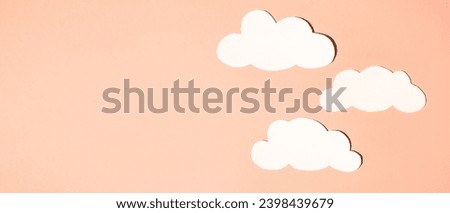 Silhouettes of clouds from white paper on a background. Banner, flat lay, place for text. Peach fuzz is color of year 2024.