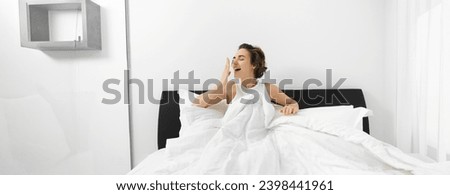 Image of smiling, beautiful modern woman wake up in her bed, yawning with pleased face, had a good night sleep.