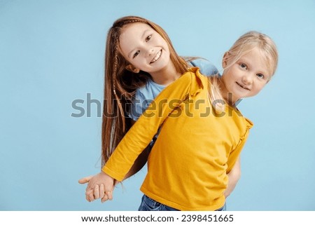 Portrait of smiling girls, cute sisters looking at camera isolated on blue background. Young happy fashion models posing for pictures in studio. Childhood, positive lifestyle concept 