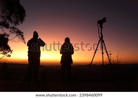 Silhouetted against the bright twilight sky, two people observe and take pictures. The colors of the sky is enhanced by the effects of the Hunga Tonga volcano, which erupted 6 months before.
