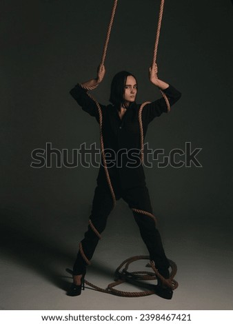 young light-skinned girl with dark bob hair in dark clothes with a rope artistic light