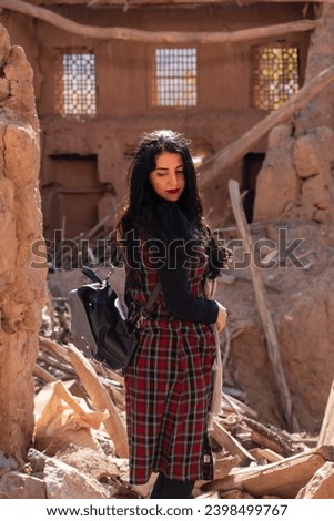 A striking image of a Middle Eastern woman with long, black hair. She stands in the midst of traditional rural walls in the central desert of Iran, dressed in modern clothing. Her hair flows down...
