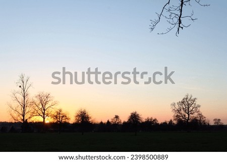 Exterior landscape view of a Countryside sunrise or sunset in Nomandy France with trees, forests and field and the horizon skyline and majestic grade gradient of colours in sky from orange blue pink