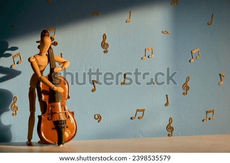 A 12 inch wooden drawing mannequin figure plays a double bass against a blue backdrop with gold musical notes and treble and bass clefs Royalty-Free Stock Photo #2398535579