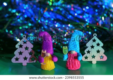 Two toy dwarfs made of plasticine with glasses of champagne on the background of Christmas decorations. New Year's holidays and Christmas. Decorations and decorations. Green background.