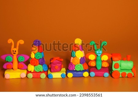 A toy Christmas train made of plasticine with gifts and Christmas trees. Bright orange background. New Year decorations.