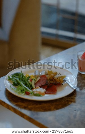 a breakfast plate with various items including scrambled eggs, sausages, roasted potatoes, slices of tomato, and a fresh green salad, presented on a marble table.