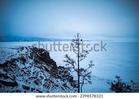 Rock montain on the shore of the frozen winter lake Baikal in cloudy foggy winter day. Winter Siberian landscape. Ogoy Island on Lake Baikal. 