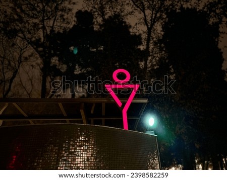 Pink neon light of men toilet symbol shape on dark park background. Free toilet in the street among trees. Restroom sign in the street. Washroom icon.