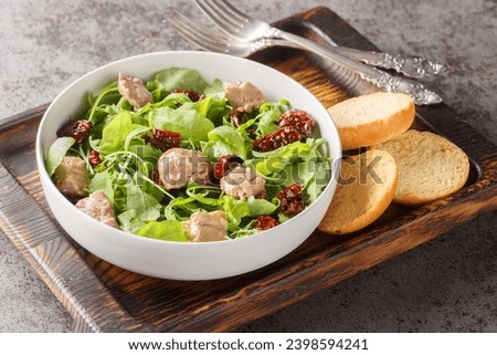 Canned cod liver salad with fresh arugula and sun-dried tomatoes served with toast close-up in a bowl on the table. Horizontal
