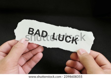 Human hand holding a paper note with word Bad Luck in dark black background.