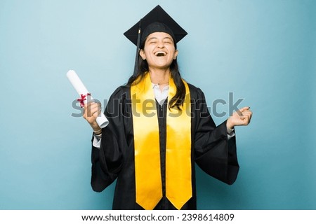 Excited hispanic university graduate celebrating finishing college and receiving her university diploma wearing her graduation gown and celebrating Royalty-Free Stock Photo #2398614809