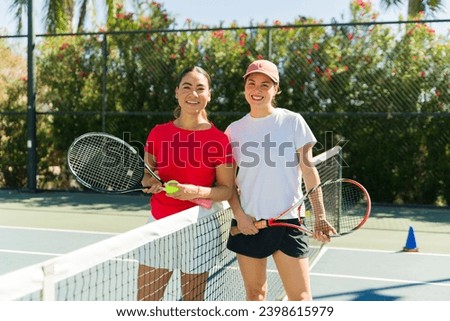 Smiling excited young women looking at the camera happy while using rackets after playing a tennis game together