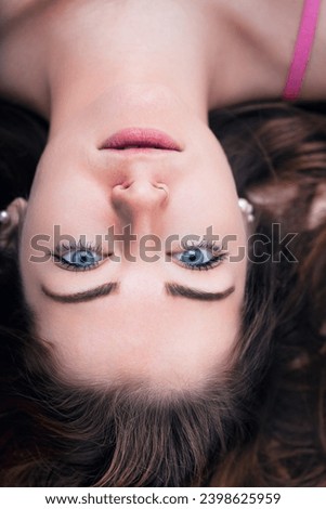 The woman's upside-down perspective adds a playful twist to her relaxed demeanor, framed by cascading waves of hair