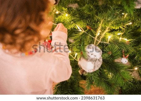 Little girl with her back turned, putting ornaments on the Christmas tree. Royalty-Free Stock Photo #2398631763
