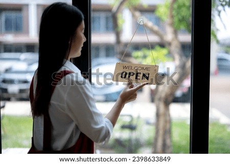 Close up of woman's hands in apron hanging a shop opening sign,  SME entrepreneurs.