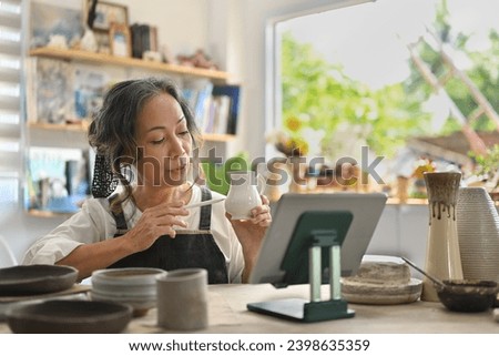 Senior craftswoman selling ceramic on the online platform with digital tablet in the art store, Small Business, and Crockery Shop concepts.