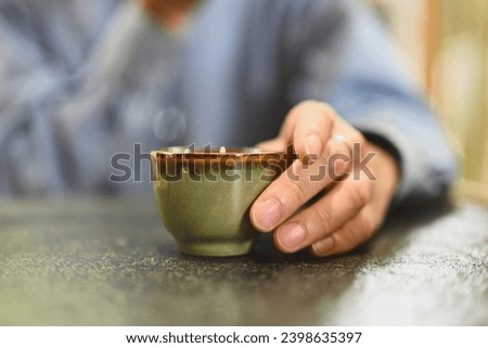 Close-up and cropped male hand holding a small cup of tea, Traditional Asian tea cup, Concept Drinking tea for health. Royalty-Free Stock Photo #2398635397