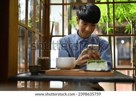 Young Asian man uses cell phone to take photos of drinks and desserts in cafe, social lifestyle concept