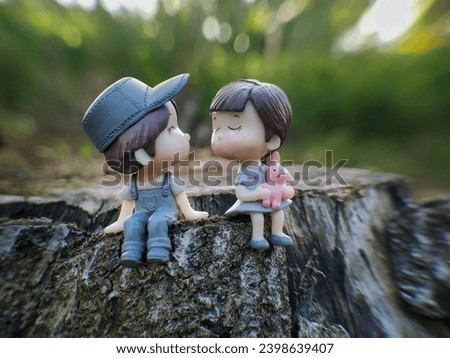 Two mini figures of a man and a woman are looking at each other and sitting on a wooden stand with a bokeh background
