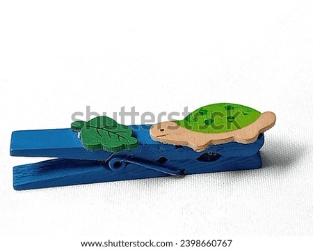 Blue clothes peg, green turtle and green leaves placed on a white background. Close -up shot of the clothes peg.