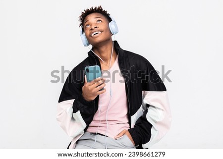 Relaxed afro american smiley guy in casual fashionable outfit clothes holding cell phone in hands using like mcrophone wearing wireless headphones listening to music enjpying shooting process.