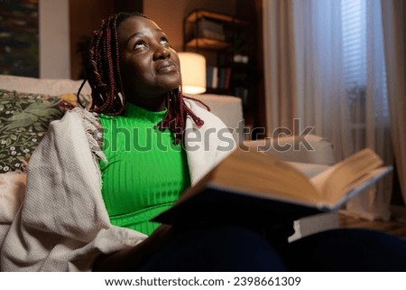Inquisitive smart afro american woman teacher tutor sitting in the living room at cozy home beautiful young lady holding reading book resting relaxing after hard day.