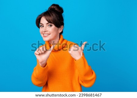 Photo of cheerful positive woman dressed orange sweater showing two thumbs back empty space isolated blue color background