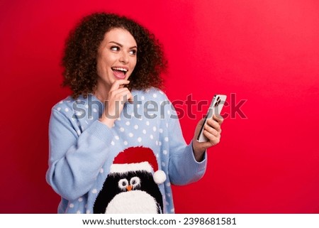 Photo of young excited girl touch chin choose best xmas surprise hold her mobile phone look novelty isolated on red color background