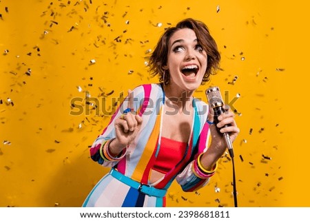 Photo of young charming girl striped overalls discotheque atmosphere point finger up microphone singing isolated on yellow color background
