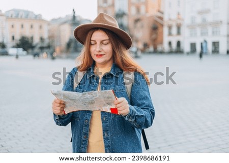 Attractive young female tourist is exploring new city. Redhead girl holding a paper map on Market Square in Krakow. Traveling Europe in autumn. St. Marys Basilica. Vacation concept