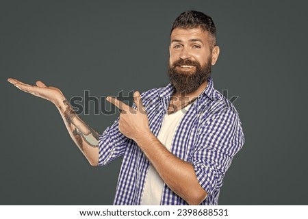 bearded man wear checkered shirt point finger on grey background with copy space