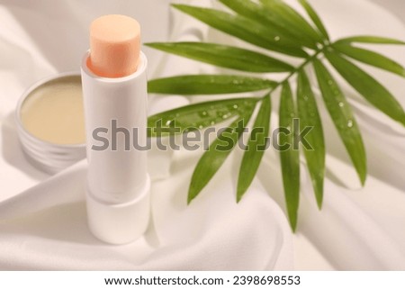 Lip balms and palm leaf on white fabric, closeup. Space for text Royalty-Free Stock Photo #2398698553