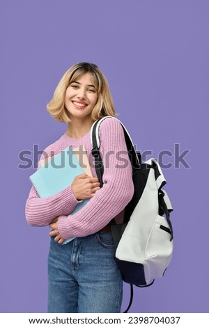 Happy pretty gen z blonde smiling girl student with short blond hair holding backpack notebooks wearing jeans pink sweater looking at camera standing isolated on purple background. Vertical portrait.